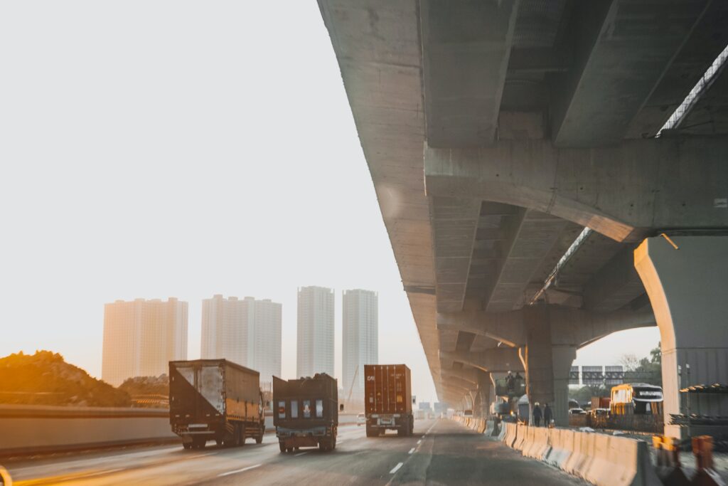 An image of freight trucks driving on a road under a bridge